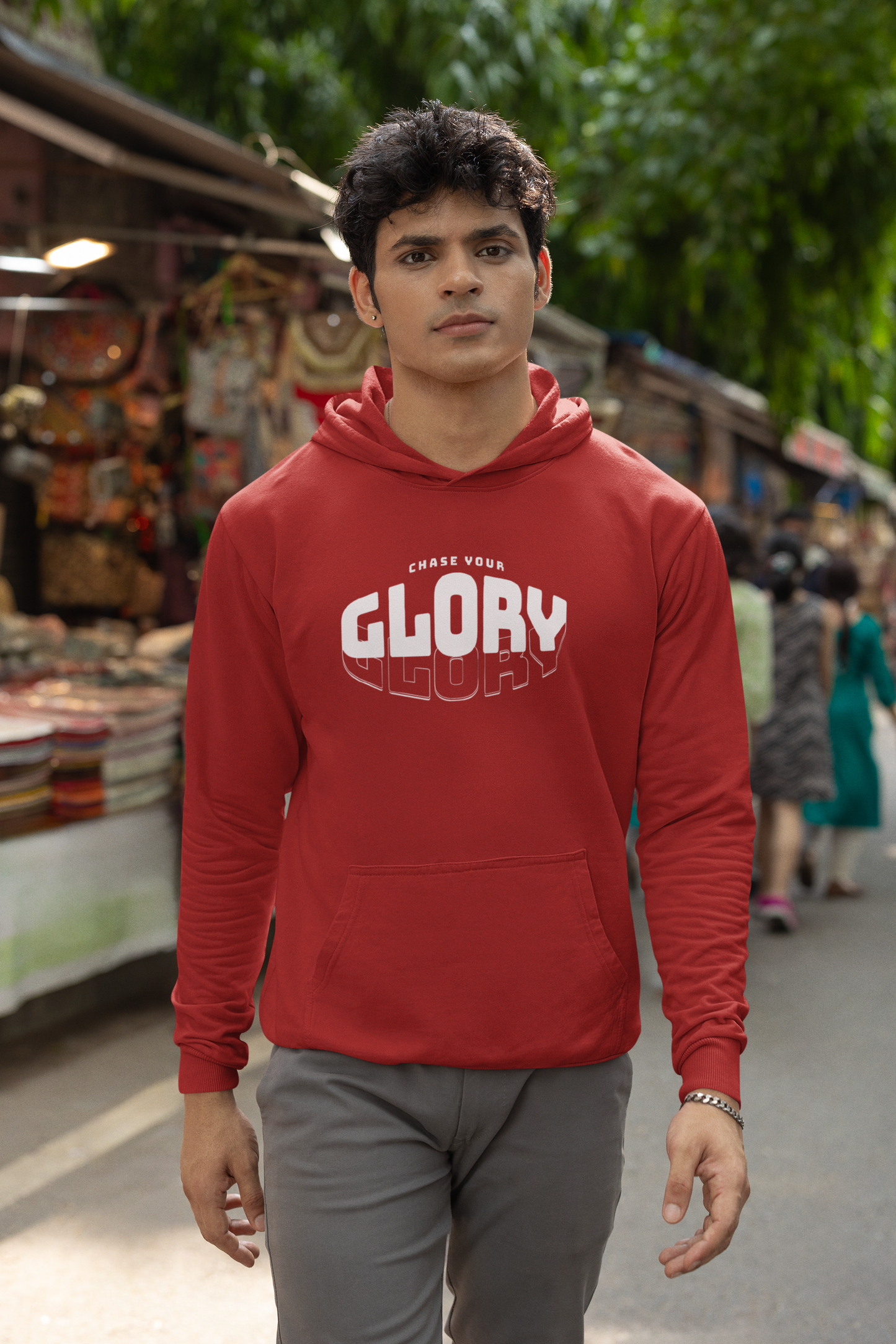 Man wearing a red hoodie with 'GLORY' printed on it, standing in an outdoor market setting.