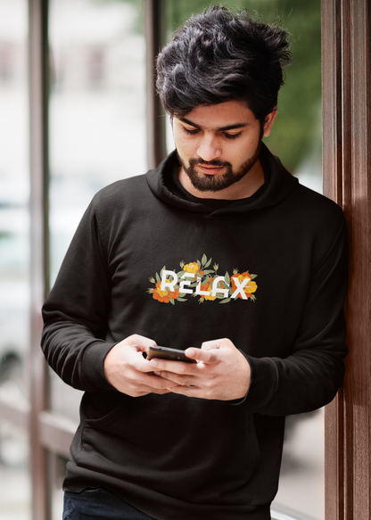 Man wearing a black hoodie with floral text design, leaning against a door.