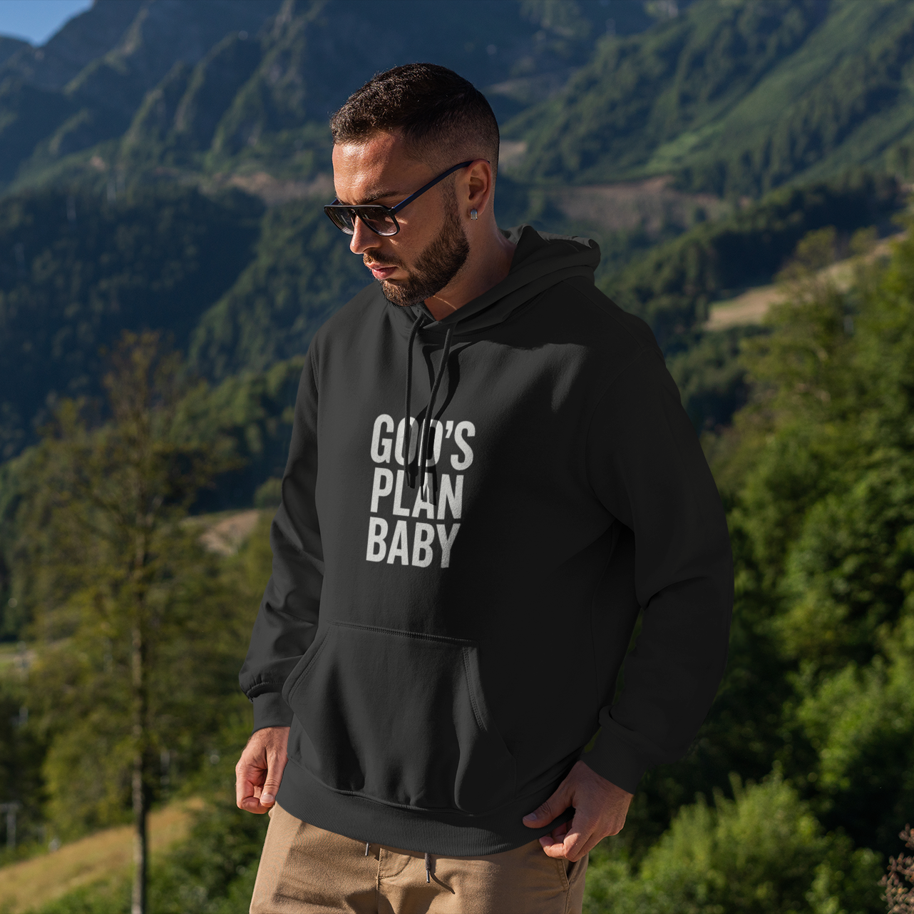 Man wearing a black hoodie with text standing in a mountainous landscape
