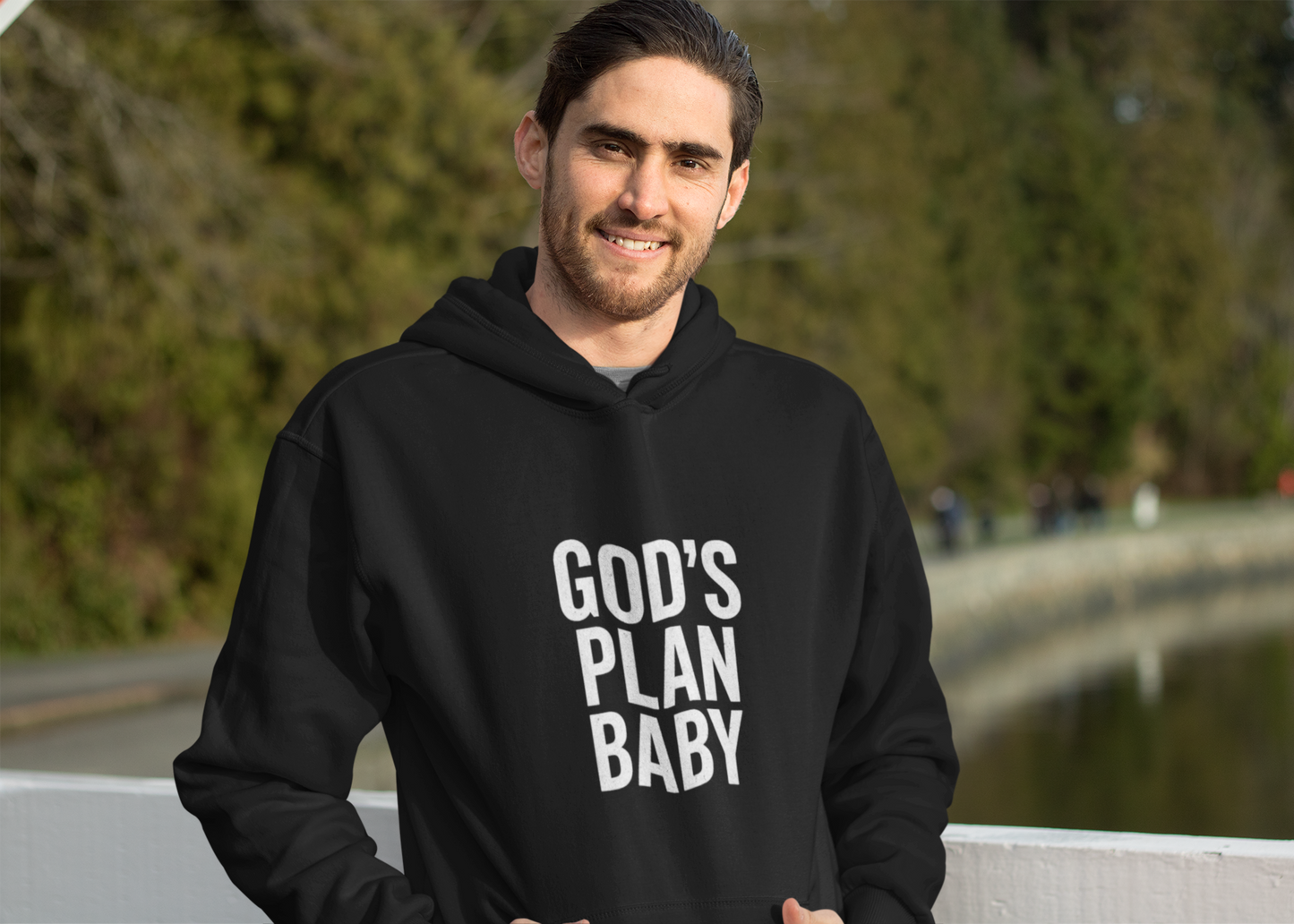 Man wearing a black hoodie with 'GOD'S PLAN BABY' text outdoors.