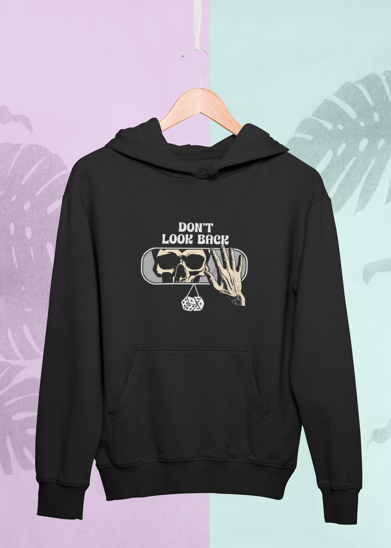 Black hoodie with graphic design on a hanger against a multicolored leaf-patterned background