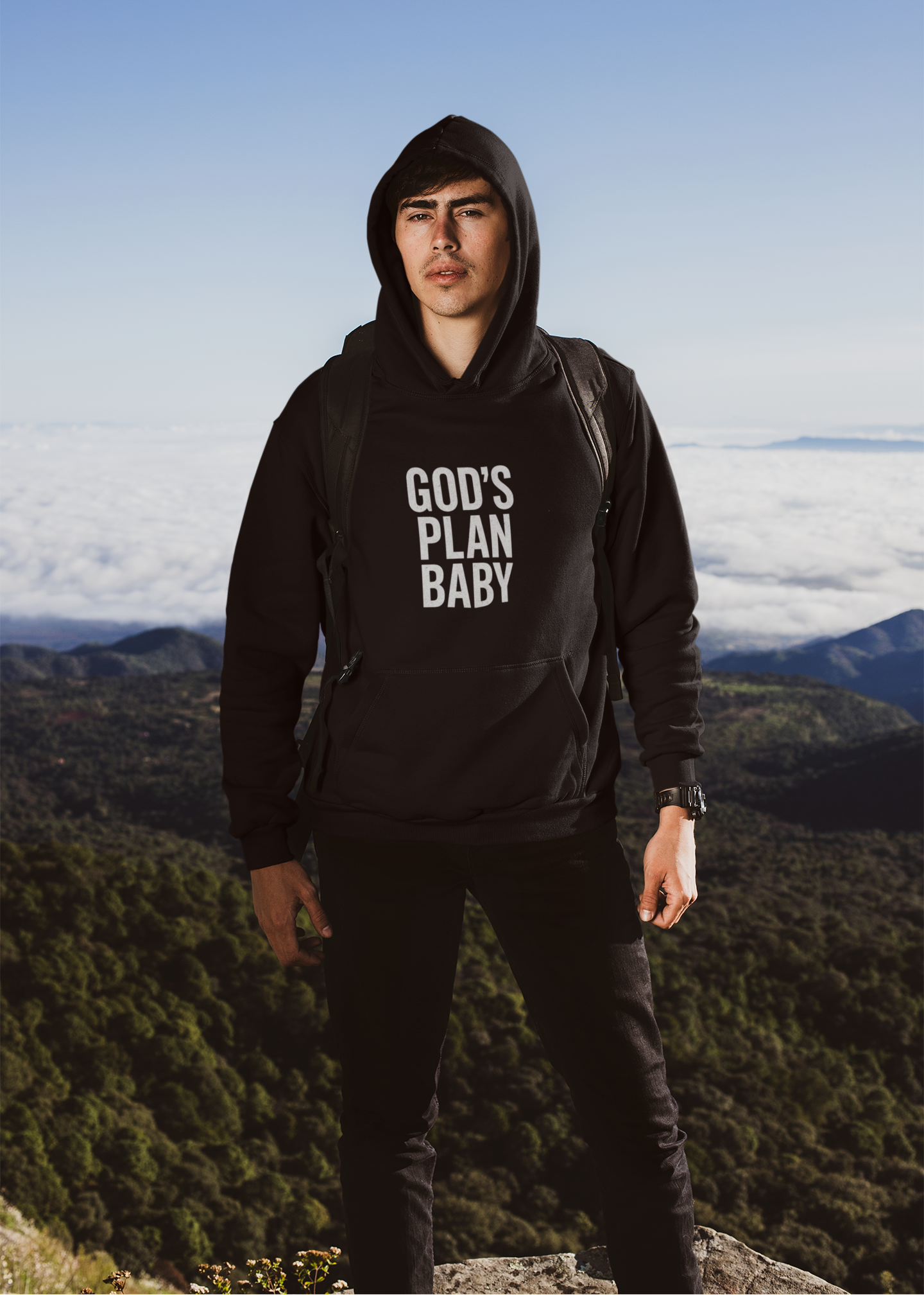 Person wearing a black hoodie with 'GOD'S PLAN BABY' text, standing on a mountain with a scenic view.